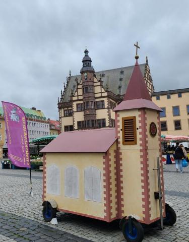 Die Wagenkirche auf dem Schweinfurter Marktplatz, im Hintergrund das Rathaus. Stark bewölkter, regnerisch wirkender Himmel.