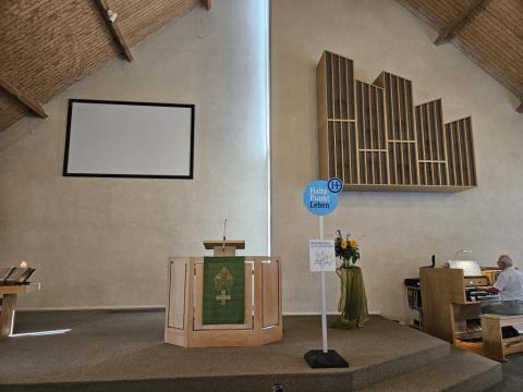 Der schlicht gehaltene Altarbereich der Kirche der Doopsgezinde Gemeente Ouddorp. In der Mitte steht ein Schild "Haltepunkt Leben", das an eine Bushaltestelle erinnert.