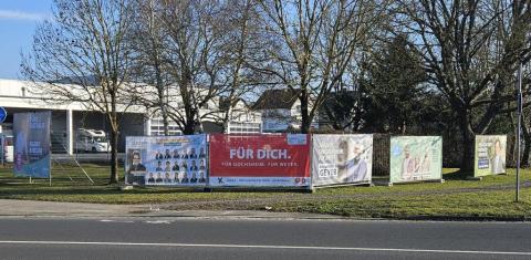 Bauzäune mit Bannern verschiedener Parteien direkt nebeneinander am Straßenrand