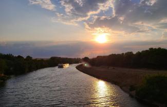 Main mit Schiff und sich spiegelnder Abendsonne