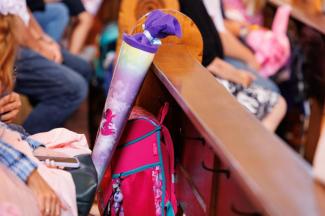 Kinder sitzen beim Einschulungsgottesdienst in einer Kirchenbank. Man sieht eine Schultasche und eine Schultüte.